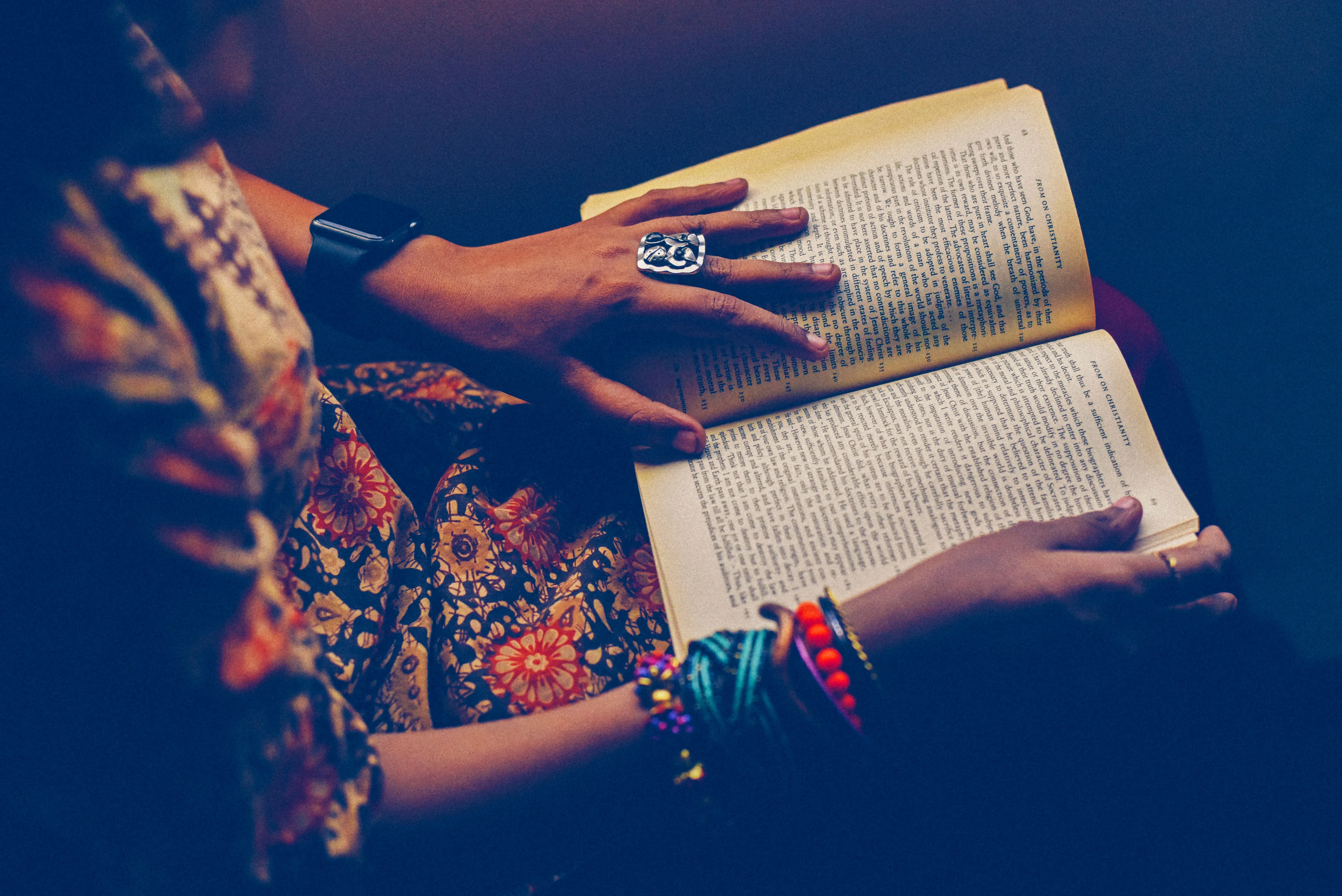 Perempuan membaca buku di pangkuan—gaya santai, cocok untuk sesi baca fokus.